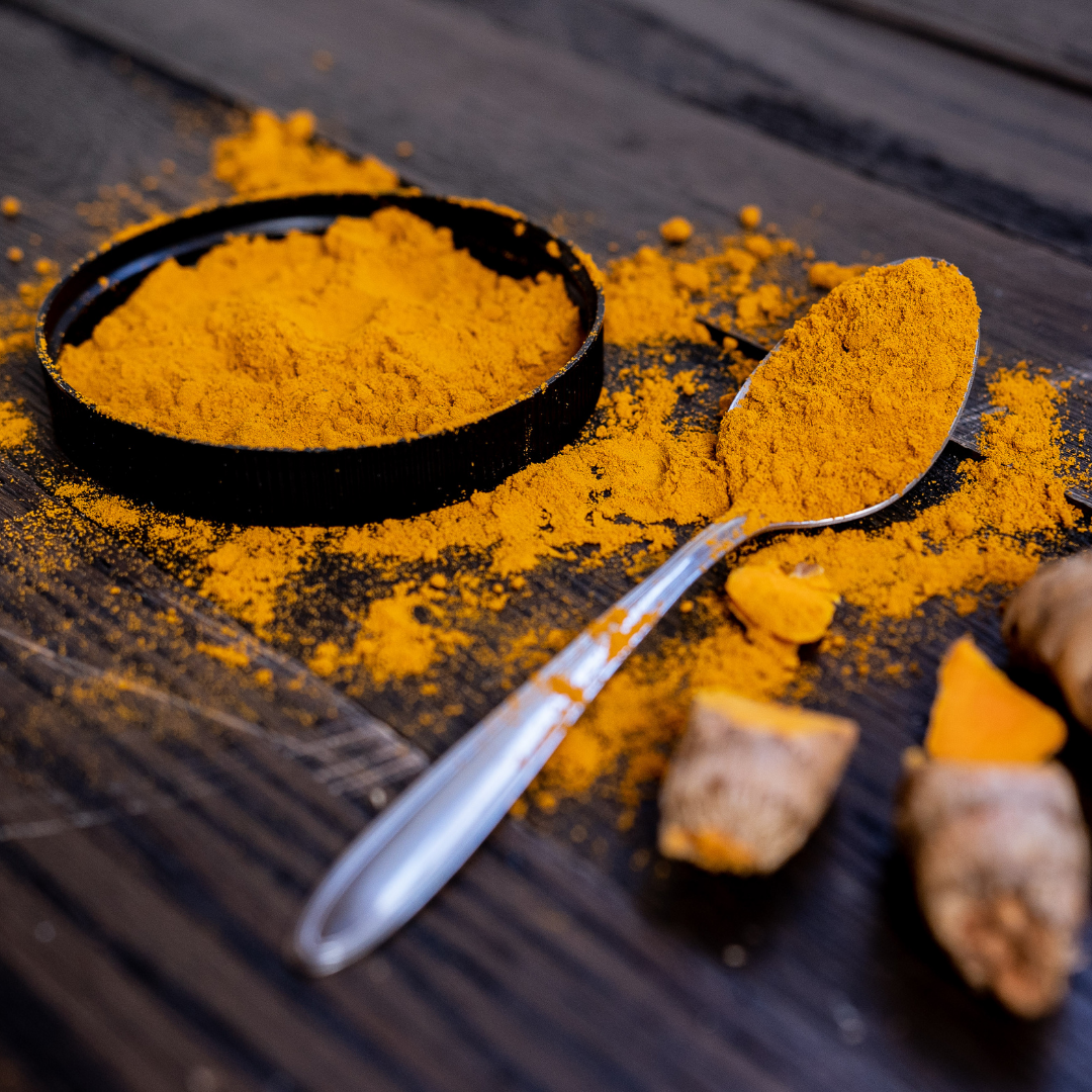 Turmeric powder on a spoon and black container on a wooden surface